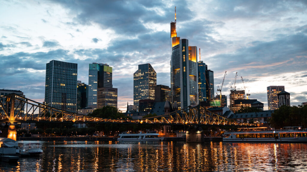 Cityscape of Frankfurt downtown at sunset, Germany. River Main with moored boats, skyscrapers with illumination on the background